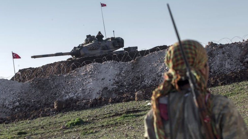 A Syrian Kurdish militia member of the YPG patrols near a Turkish army tank in Aleppo province, Syria (22 February 2015)