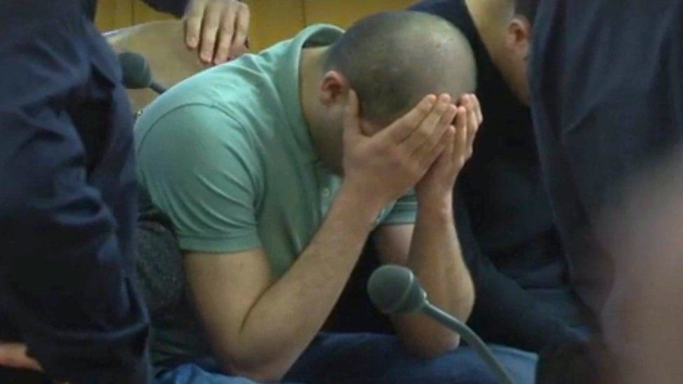 A defendant covers his face at the beginning of his trial on gang-raping a German tourist in Vienna, Austria