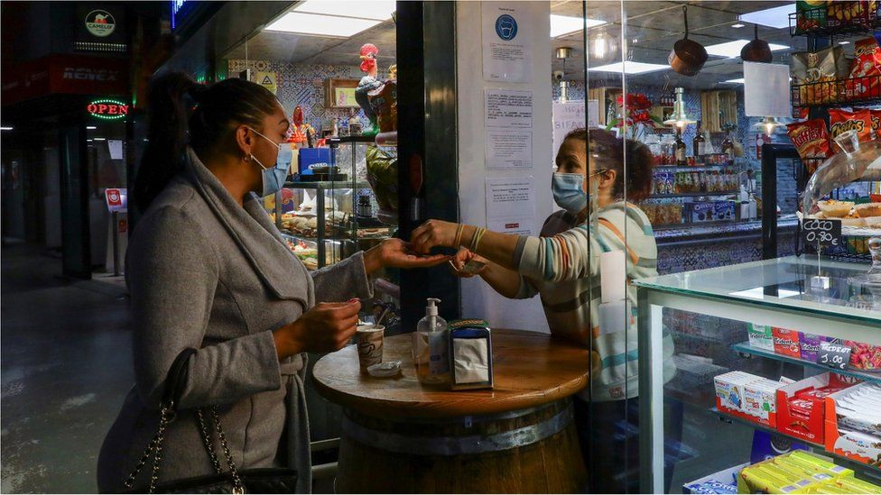 Женщина покупает кофе у входа в частично открывшееся кафе в соответствии с планом правительства Португалии по постепенному снятию ограничений, введенных в середине января для борьбы с всплеском на тот момент наихудшим в мире коронавирусом (COVID-19), в Порту, Португалия. 15 марта 2021 года.