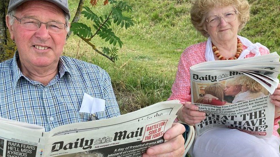 man and woman sitting in fold-up chair reading the Daily Mail