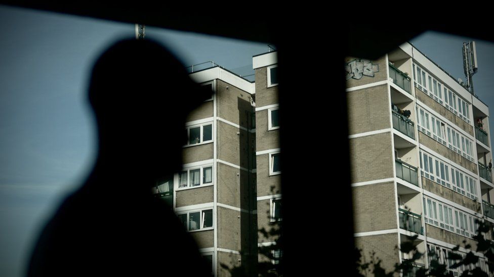 A silhouette of a man in front of a view of tower blocks in London