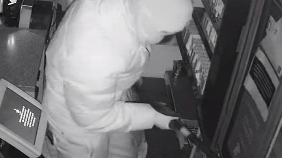 Suspect breaking into the tobacco and cigarette cabinet with a bar