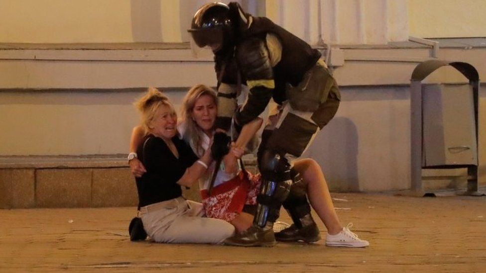 A riot police officer tries to move two women sitting on the pavement in Minsk, Belarus. Photo: 10 August 2020