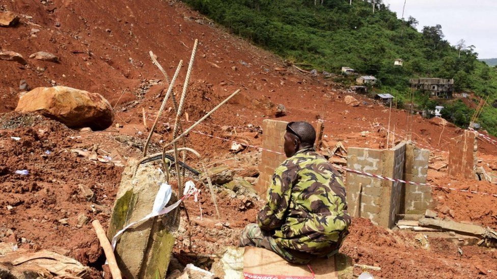 A soldier sits next to a partially-collapsed hillside in Freetown
