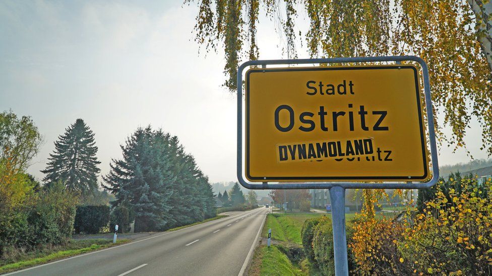 Ostritz town sign, defaced with a stencil reading "dynamoland"
