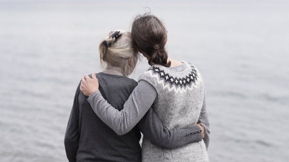 Older and younger woman embracing by the sea - posed by models