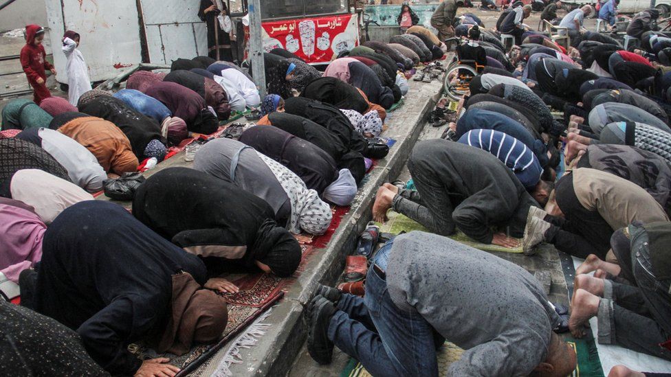 Dozens of people bowing their heads to the ground in prayer in Gaza marking Eid-al-Fitr