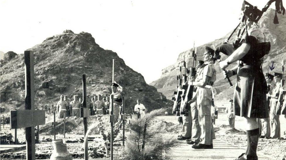 Soldiers stand to attention by open graves