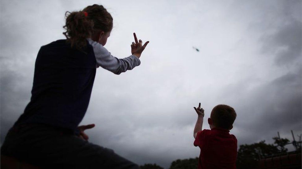 Traveller children look up and gesture as a police helicopter hovers over Dale Farm camp