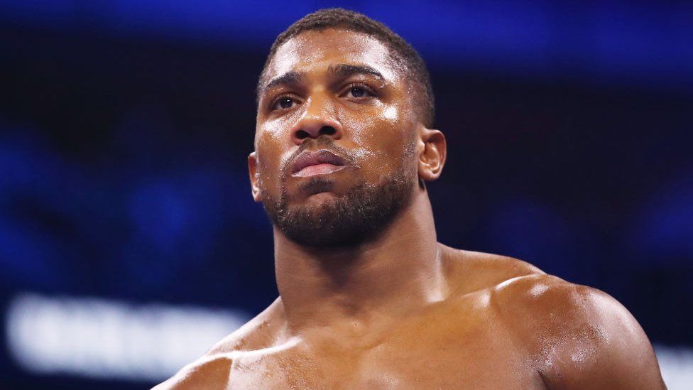 Anthony Joshua looks on prior to the Heavyweight fight between Anthony Joshua and Jermaine Franklin at The O2 Arena on April 01, 2023 in London. Joshua is a 22-year-old black man with his hair cropped short and a short beard. He has brown eyes and a muscular physique. He is photographed with a serious expression in the boxing ring and is topless and shiny with what appears to be sweat.