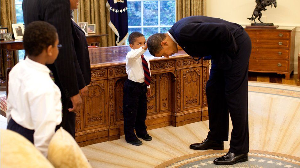 President Barack Obama bends over so the son of a White House staff member can pat his head during a visit to the Oval Office May 8, 2009.