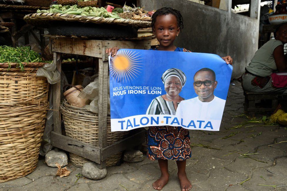 Ребенок держит плакат кампании с фотографиями действующего президента Бенина Патриса Тэлона (справа на плакате) и его напарника Мариам Талата (слева на плакате) на рынке в Котону 8 апреля 2021 года.