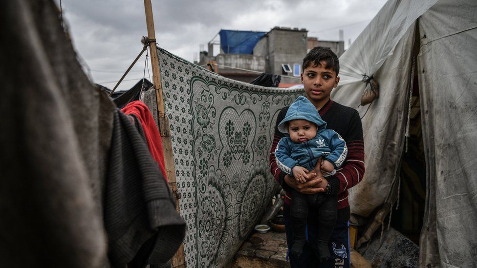 14-year-old boy and 6-month-old baby brother outside tent in Rafah