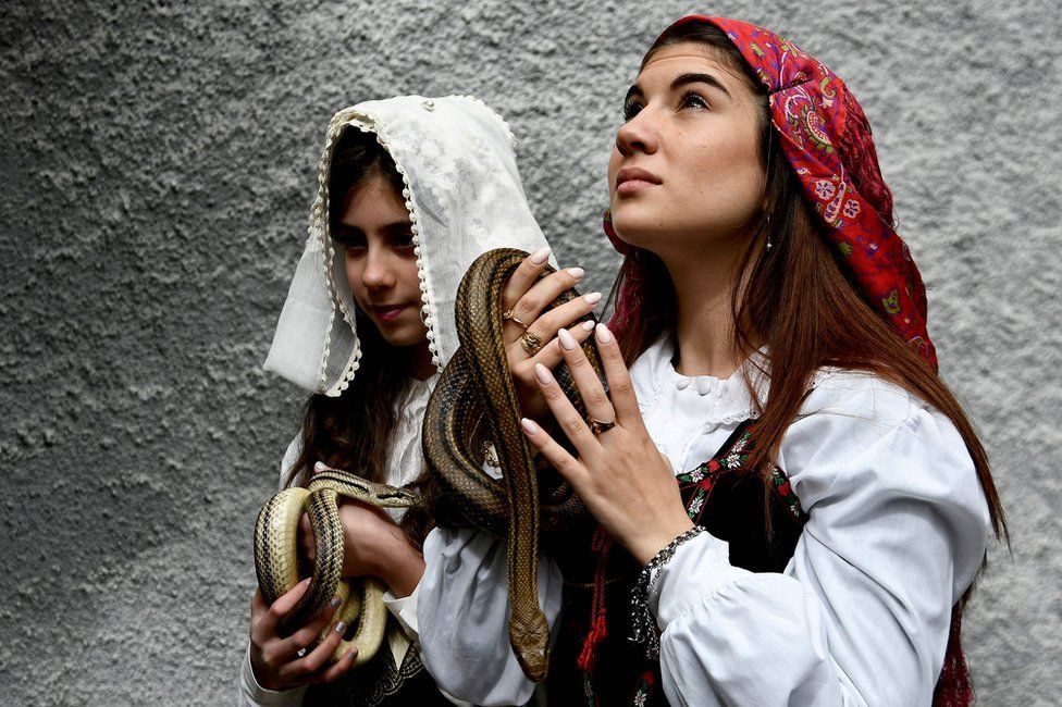 Faithfuls in traditional clothing hold snakes to place them on the statue of Saint Domenico during an annual procession in the streets of Cocullo
