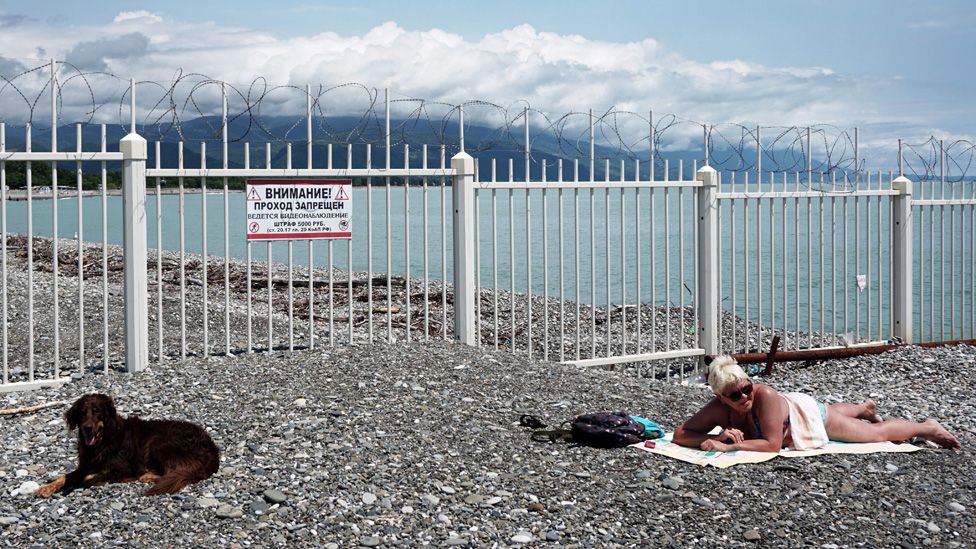 A woman and her dog sunbathe next to the Black Sea border between Russia and Abkhazia