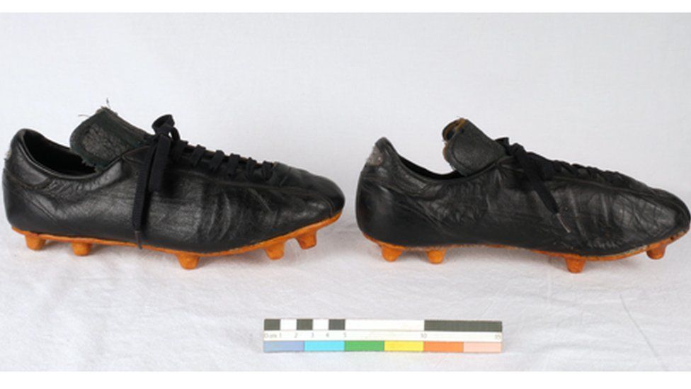 Two old football boots, black aged leather with black laces and a slightly orange-coloured sole with studs