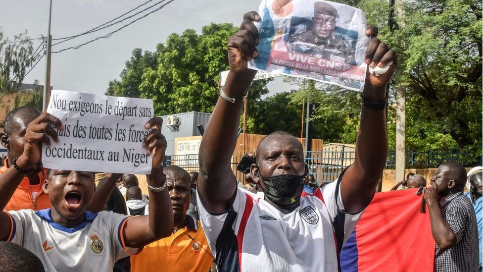 Сторонник держит фотографию нигерского генерала Абдурахамана Тиани, начальника могущественной президентской гвардии, вместе с другими участниками митинга в поддержку нигерийской хунты в Ниамее 30 июля 2023 г.