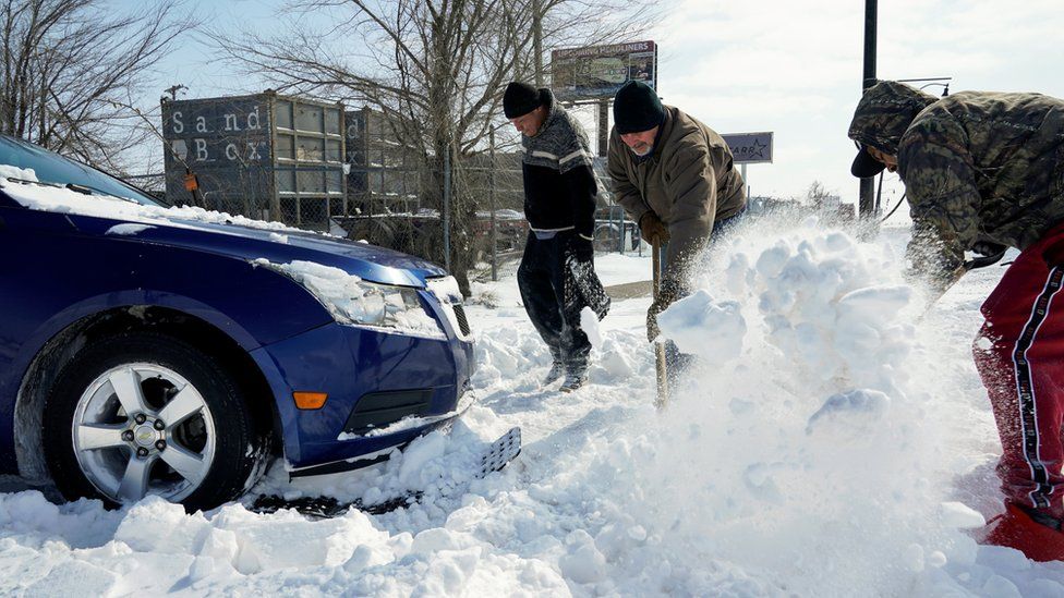 People work to free a car stuck in the snow during record breaking cold weather in Oklahoma City, Oklahoma, U.S., February 15, 2021.