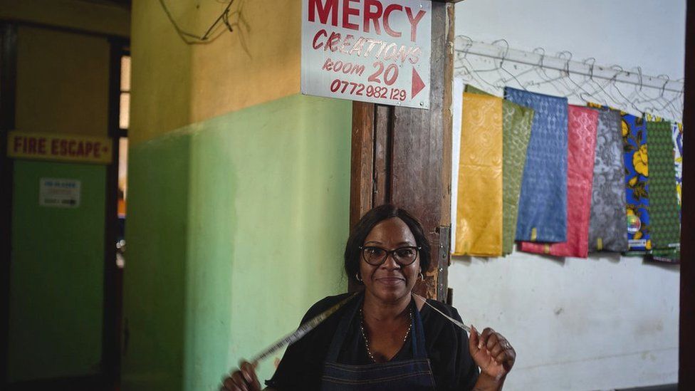 Mercy Tafirenyika beneath her shop sign with a tape measure round her neck