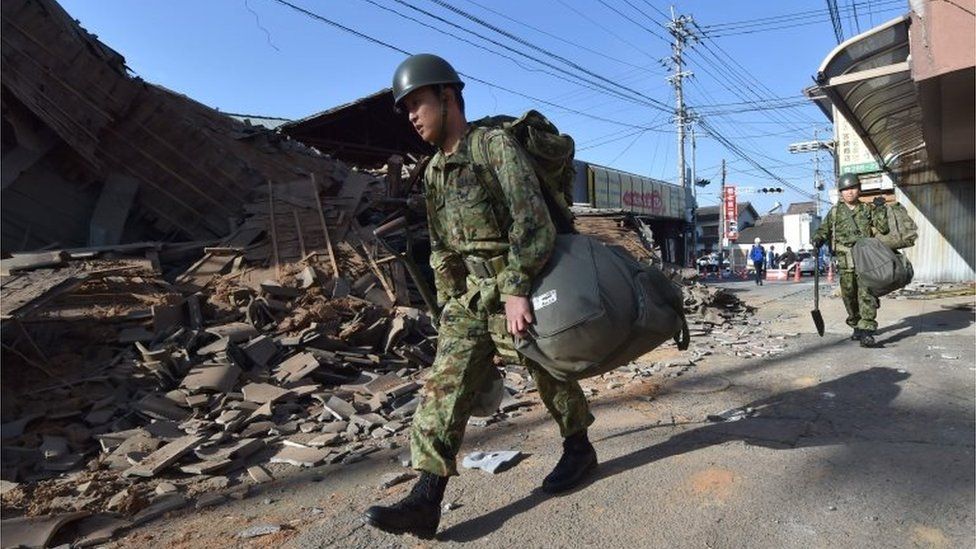 Members of Japan's self-defence forces walk past collapsed houses in Mashiki. Photo: 16 April 2016