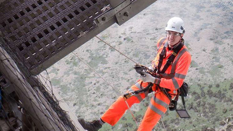 Picture looks down on a workman abseiling high above the ground, suspended from the bridge.