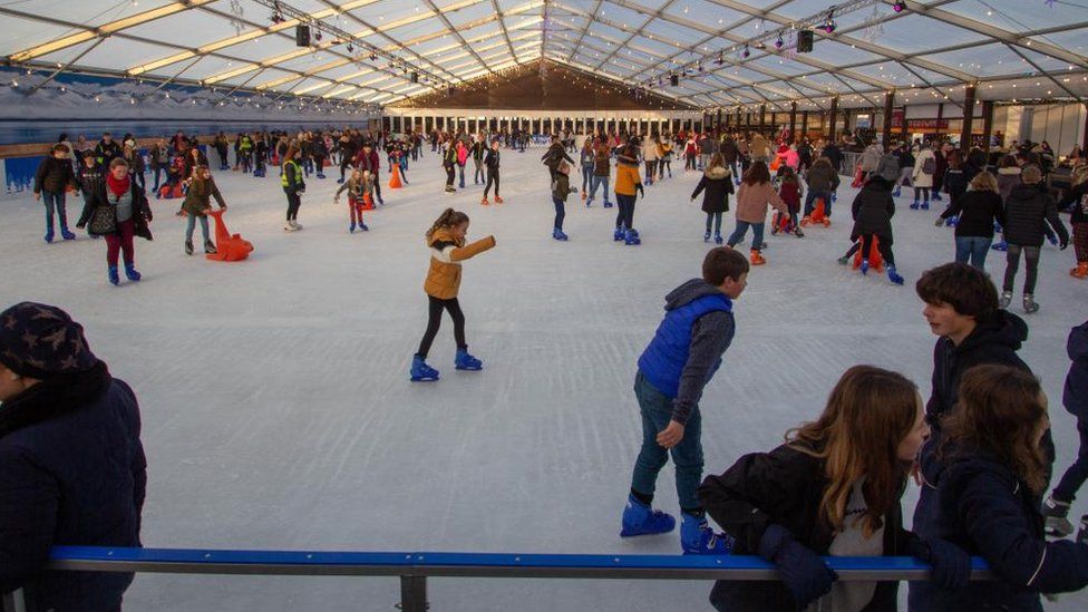 Skaters on a covered ice rink with clear roof