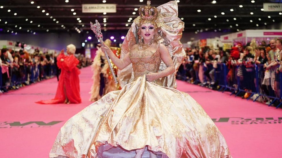 A drag queen in a crown on the pink carpet