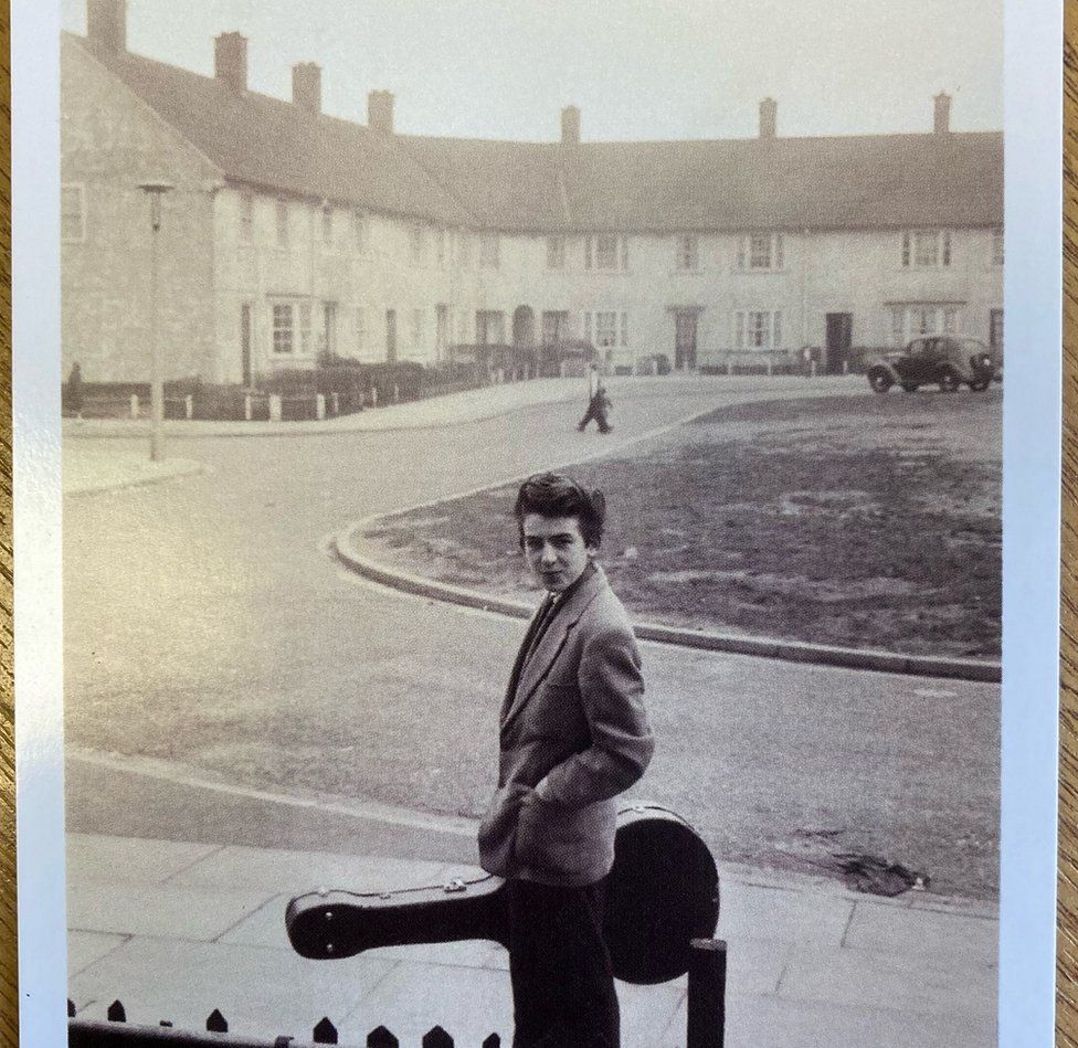 Një i ri Xhorxh Harrison duke mbajtur një kuti kitare jashtë shtëpisë së tij Speke