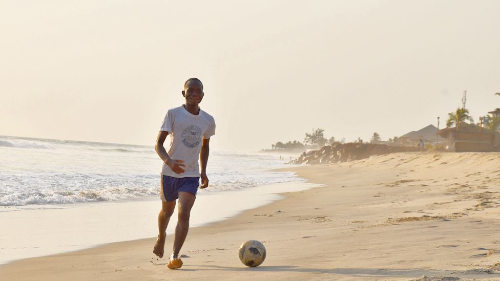 A young man playing football on a beach in Monrovia