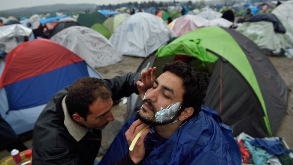 A migrant shaves another at a makeshift camp at the Greek-Macedonian border, near the Greek village of Idomeni