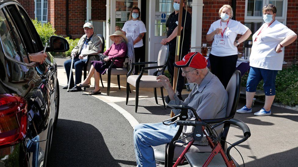 Staff look on as a visitor uses her phone to take a picture of her grandad during a drive-through visit at Gracewell, a residential care home in Adderbury near Banbury, west of London on May 28