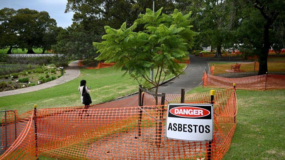 A person walks past an asbestos sign that is displayed at Victoria Park