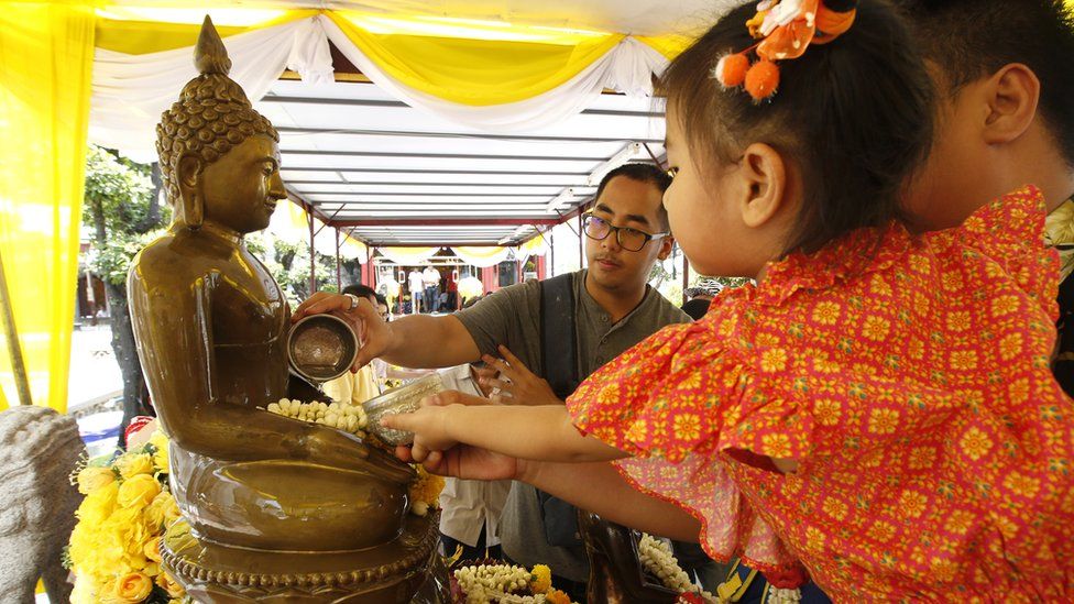 People pour scented water over a statue of a Buddha