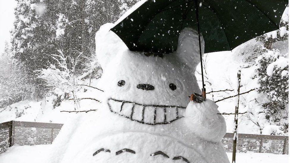 A Totoro made of snow, carrying an umbrella.