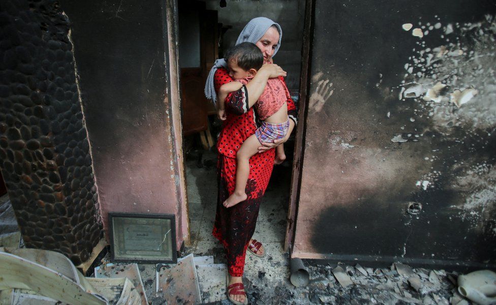 A woman carrying a child in a burnt house on 25 July 2023.