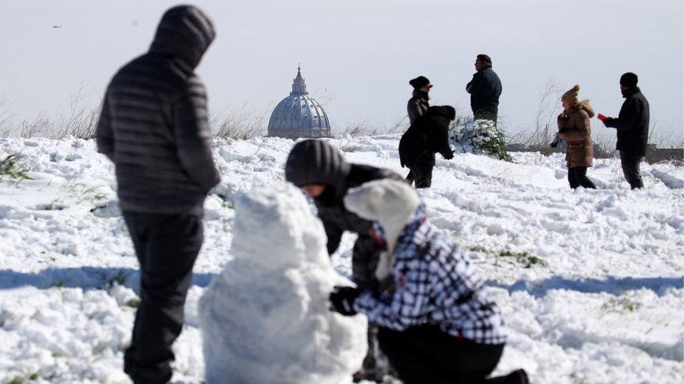 St Peter's Basilica is seen in the background as people enjoy the snow at the Circus Maximus in Rome