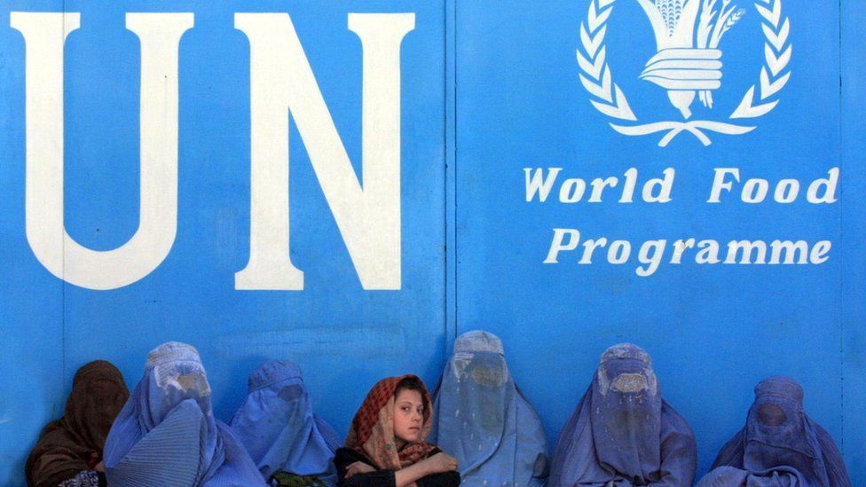 Afghan women sit in front of a United Nations sign