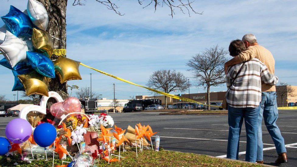 A couple hug by a memorial of flowers, balloons and candle set up by a tree across the Walmart where the shooting took place in Chesapeake, Virginia.