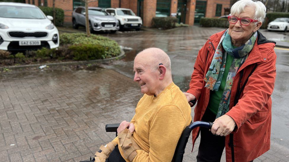 Harold being pushed in a wheel chair through a car park