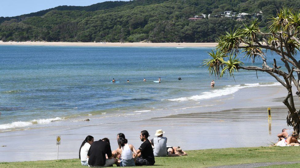 Socially-distanced groups sit on the grass near Byron Bay