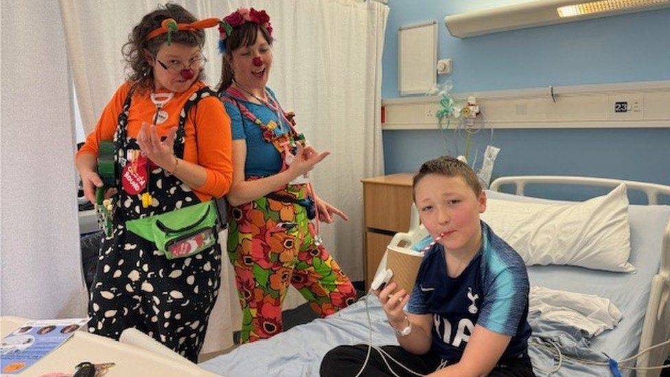 Two clowns on a ward in the Jenny Lind Children's Hospital with a young patient