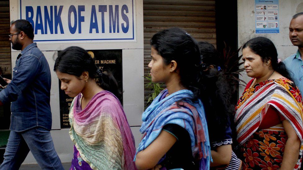 Women walk past an ATM in India in 2016