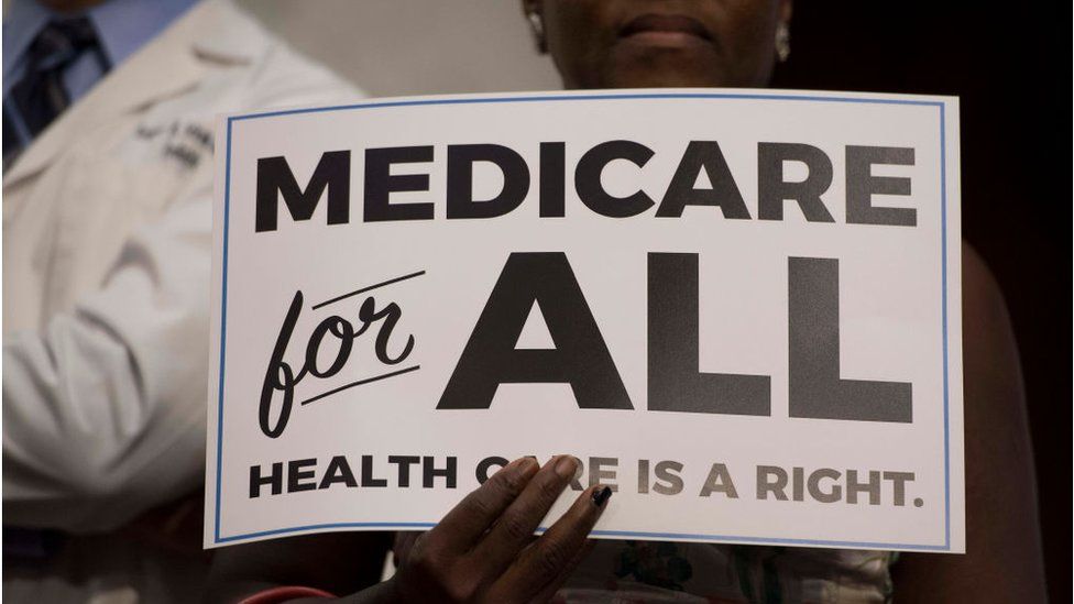 Woman holds sign reading Medicare for All - Healthcare is a right