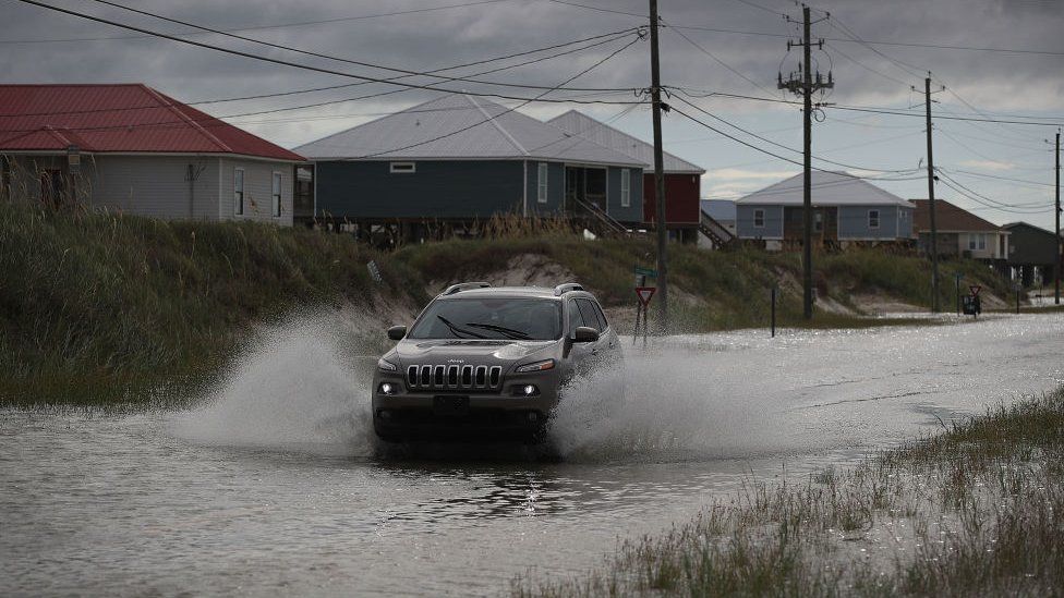 A car drives on a flooded road in Dauphin Island, Alabama