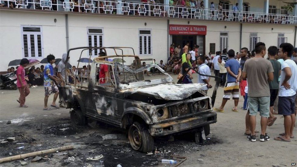 People gather near a damaged vehicle after it was set on fire during a protest in Manipur, India, Tuesday, Sept. 1, 2015