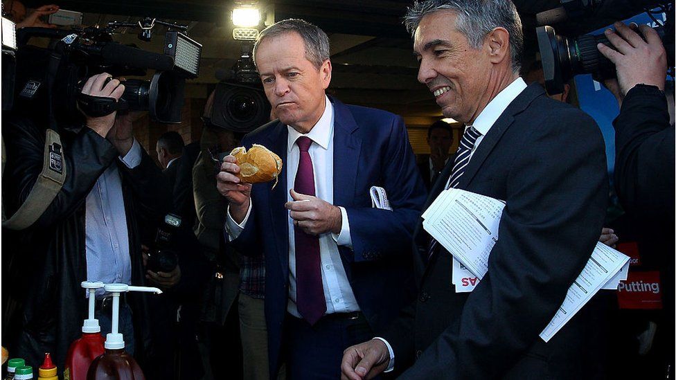 Bill Shorten takes a bite from a bun containing a sausage
