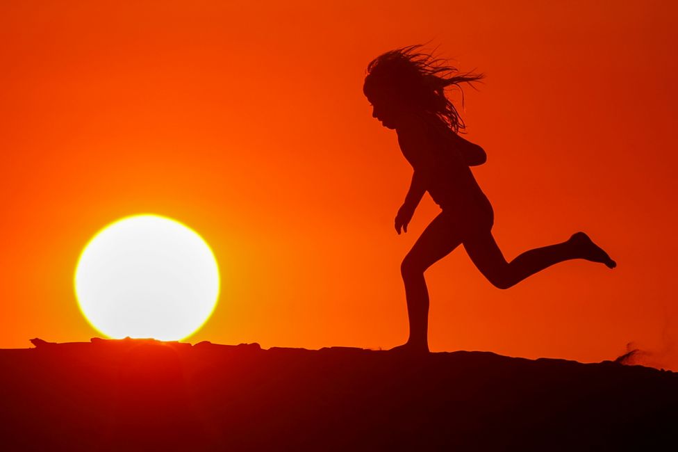 A running child is silhouetted against a red sunset