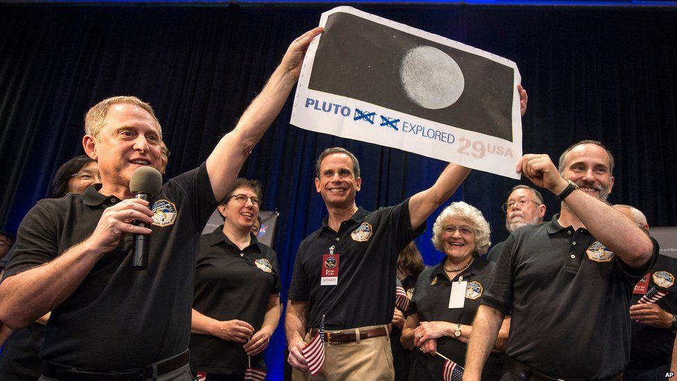 Scientists and engineers hold up an enlargement of a US postal stamp depicting Pluto