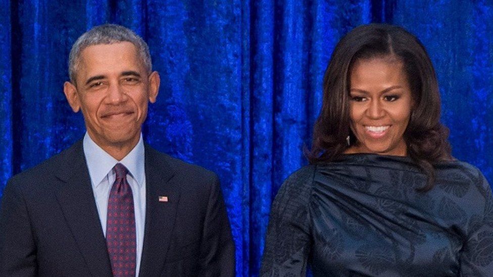 Barack and Michelle Obama stand beside each other smiling.