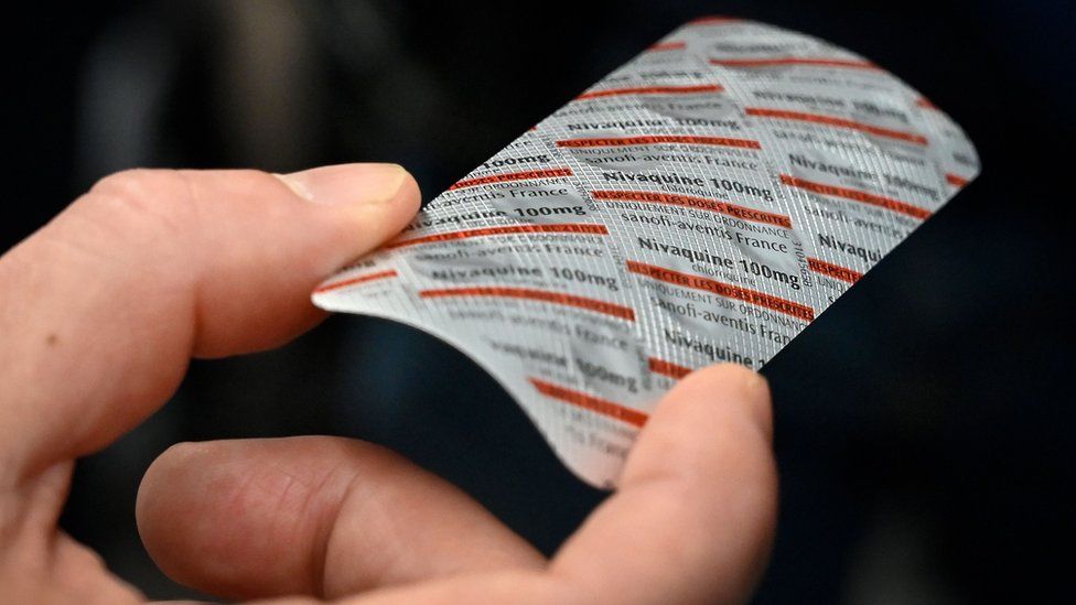 A hand holding a packet of Nivaquine, tablets containing chloroquine